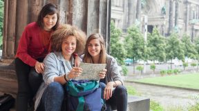 Three international students sit with a map in the courtyard of the Altes Museum in front of the Berlin Cathedral.