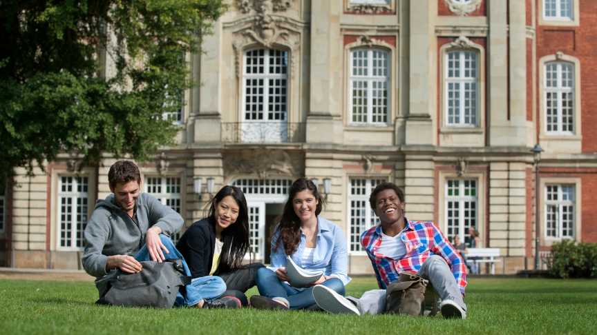 International students sit on the grass in front of the University of Bonn.