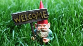A garden gnome holds up a sign with the word Welcome.